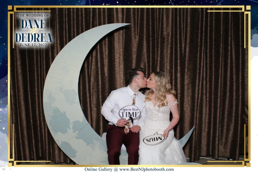 Dedrea and Dane kiss on the life-size moon photo booth at Valenzano Winery in Shamong, NJ