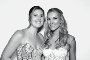 Two young women in elegant dresses smiling in a black and white event portrait at Milestone NJ.