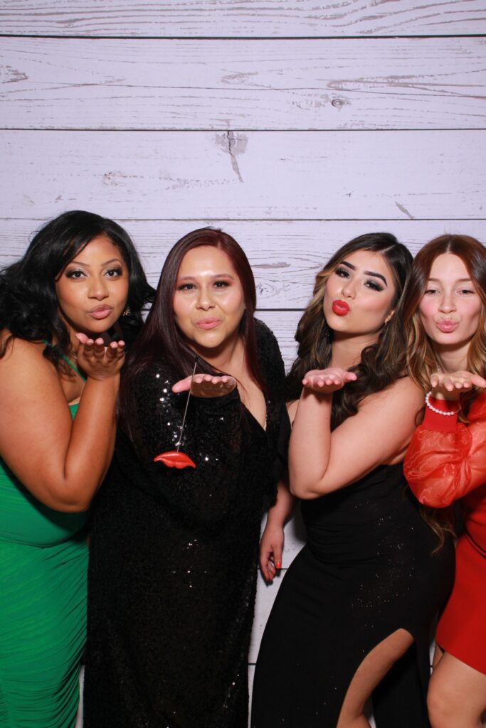 A trio of women dressed in formal gowns, sipping wine while posing for a holiday celebration photo booth at Milestone NJ.