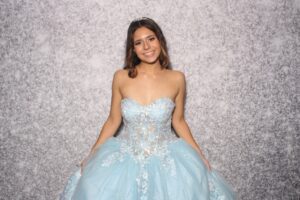 A young woman in a light blue ball gown smiling elegantly in front of a floral backdrop at Milestone NJ.