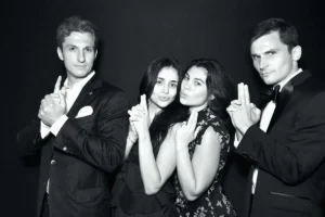 A group of four friends in formal attire striking a playful pose in front of a black backdrop at Milestone NJ.