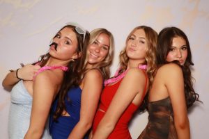 A group of women dressed in red and blue dresses posing playfully in front of a backdrop at Milestone NJ.