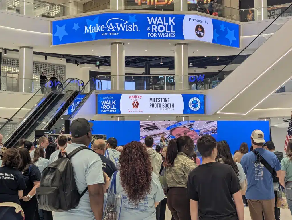 Crowd gathered at the Make-A-Wish New Jersey Walk & Roll For Wishes event at American Dream with event signage and sponsor displays
