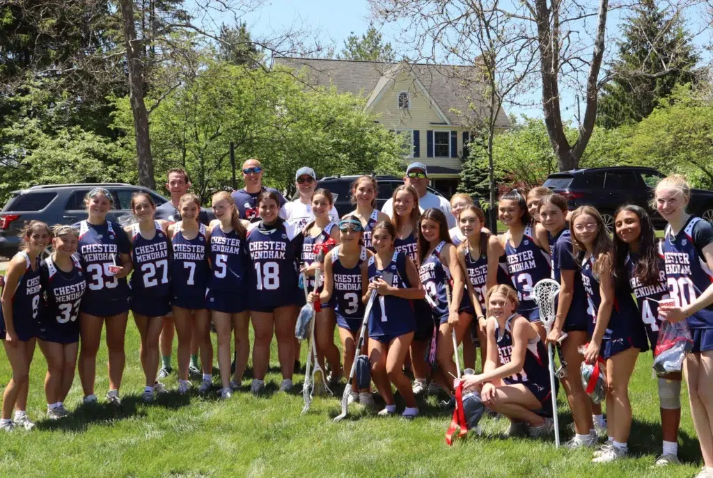 Chester Mendham lacrosse team and coaches posing together with sticks on a sunny field at CM LAX Day in Mendham, NJ