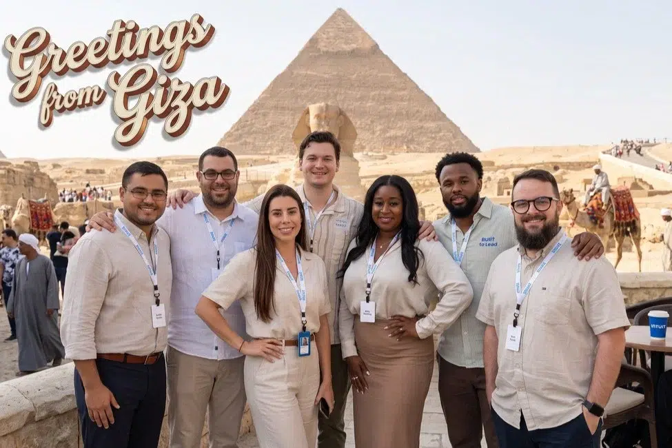 Eight Intuit team members with event lanyards at the Great Pyramid of Giza in an AI photo booth image with a Greetings from Giza title